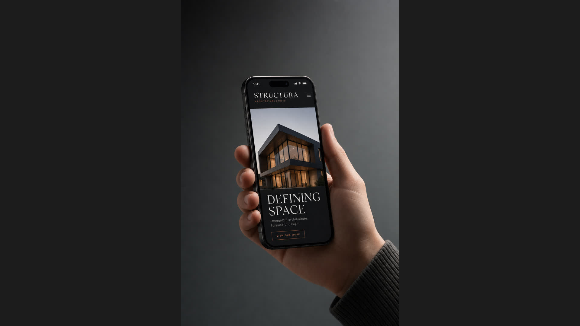 Mobilna wersja strony Structura w iPhone'ie trzymanym w dłoni: hasło DEFINING SPACE, betonowy budynek, miedziane akcenty nawigacji